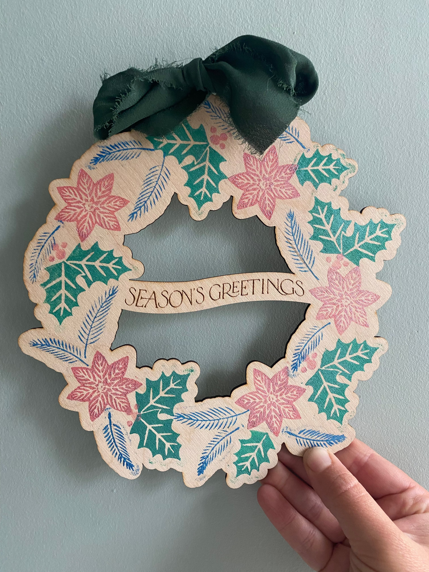 Decorative wreath Christmas decoration with winter floral designs and 'Season's Greetings' text.